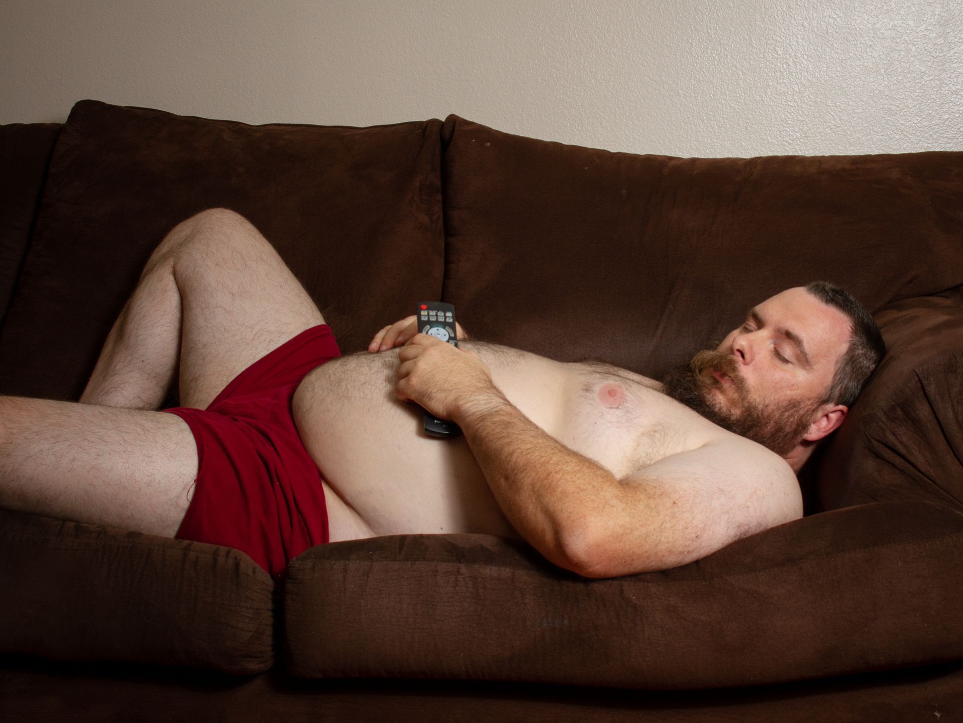A lazy man laying on the couch with a TV remote in his hand