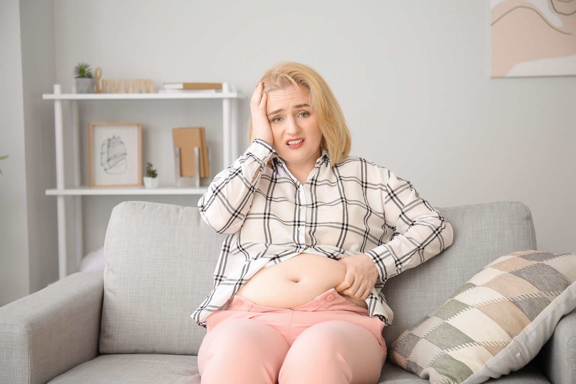 A white woman sitting on the couch with her belly hanging out.