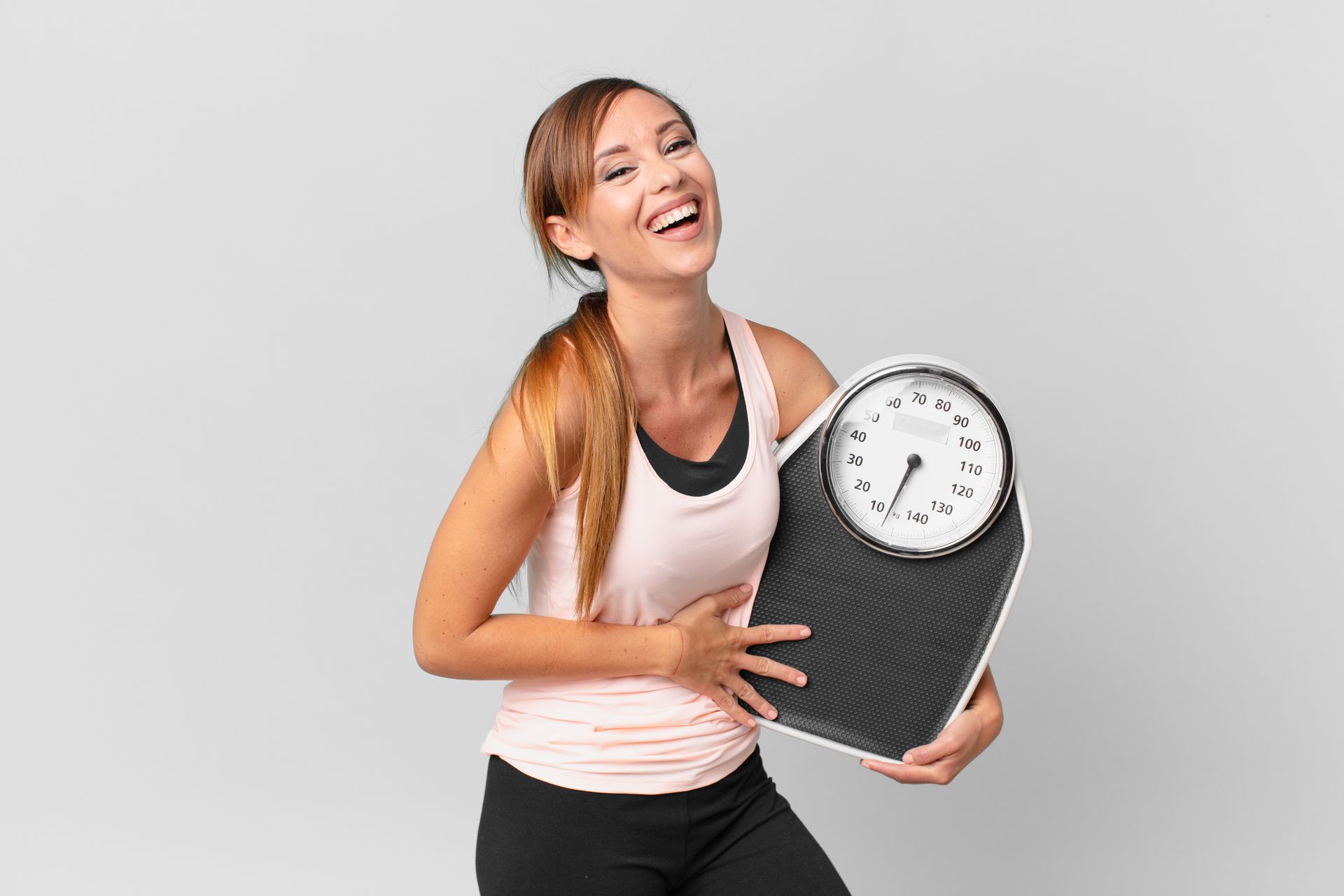 A fit white woman holding a scale laughing