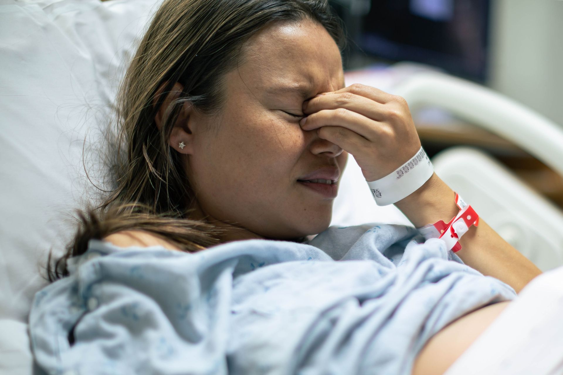 A sick woman laying in a hospital bed holding her face with her left hand