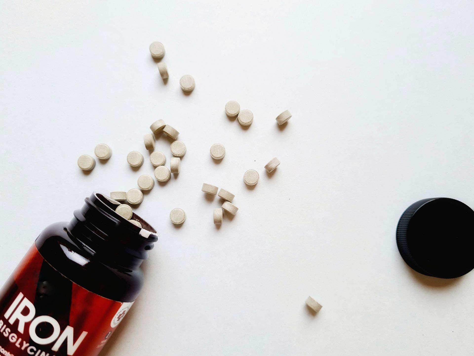 A black supplement bottle laying on a white table with white supplement pills spilling out of it