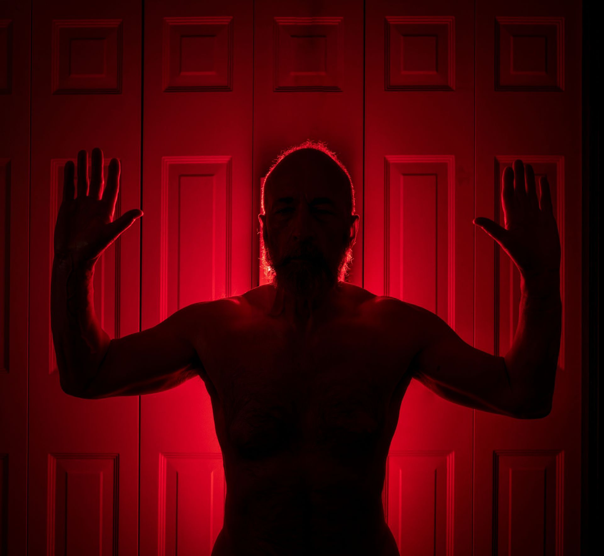 The black silhouette of a man standing in front of white closet doors with red light around him