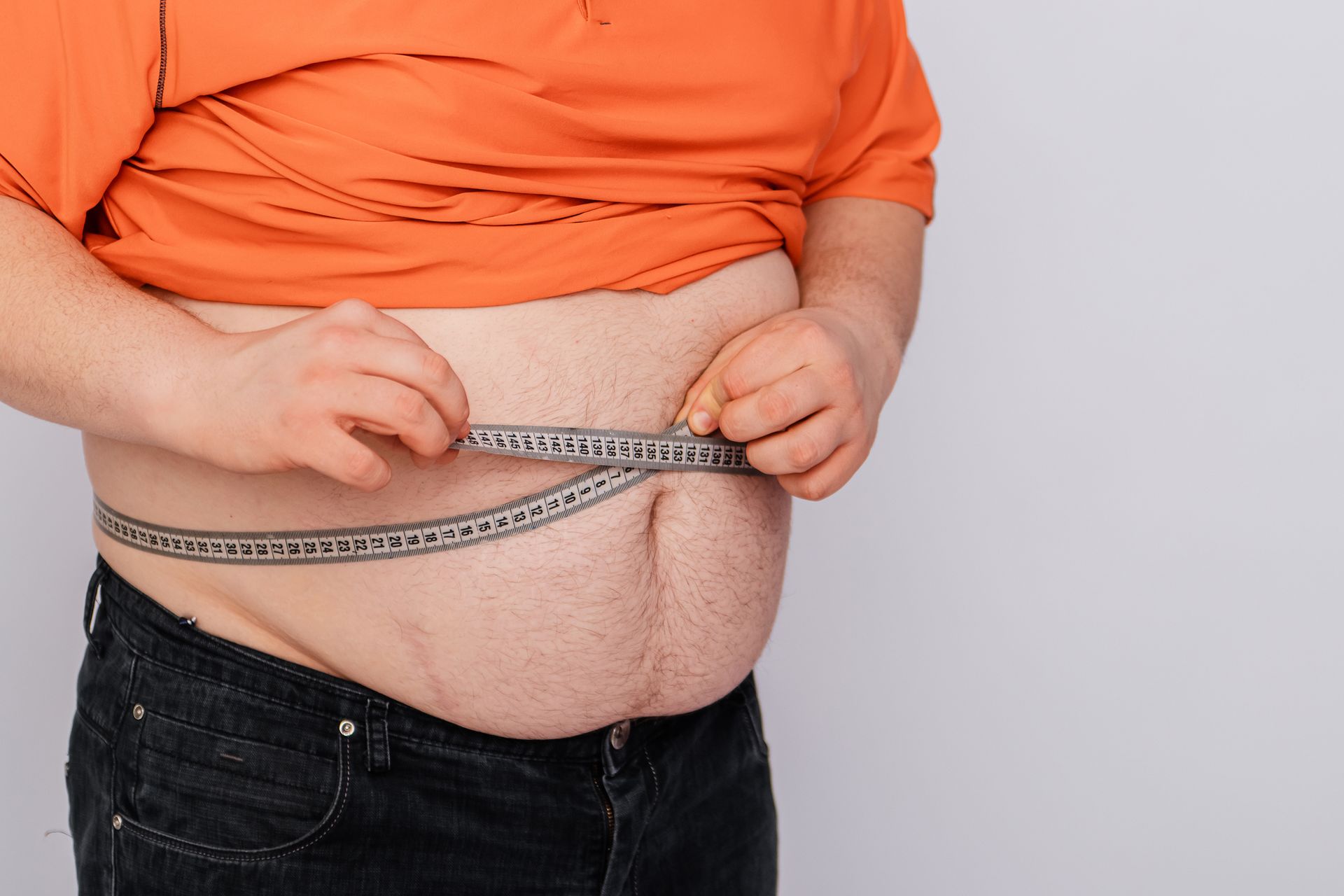 A white man wearing an orange shirt pulled up showing his belly, with a tape measure around his belly