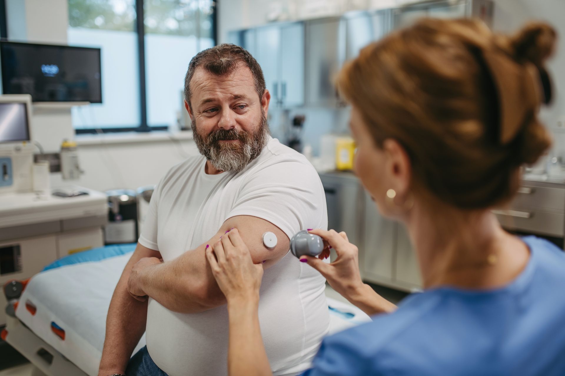 A female doctor applying a blood glucose monitor to the arm of a white man