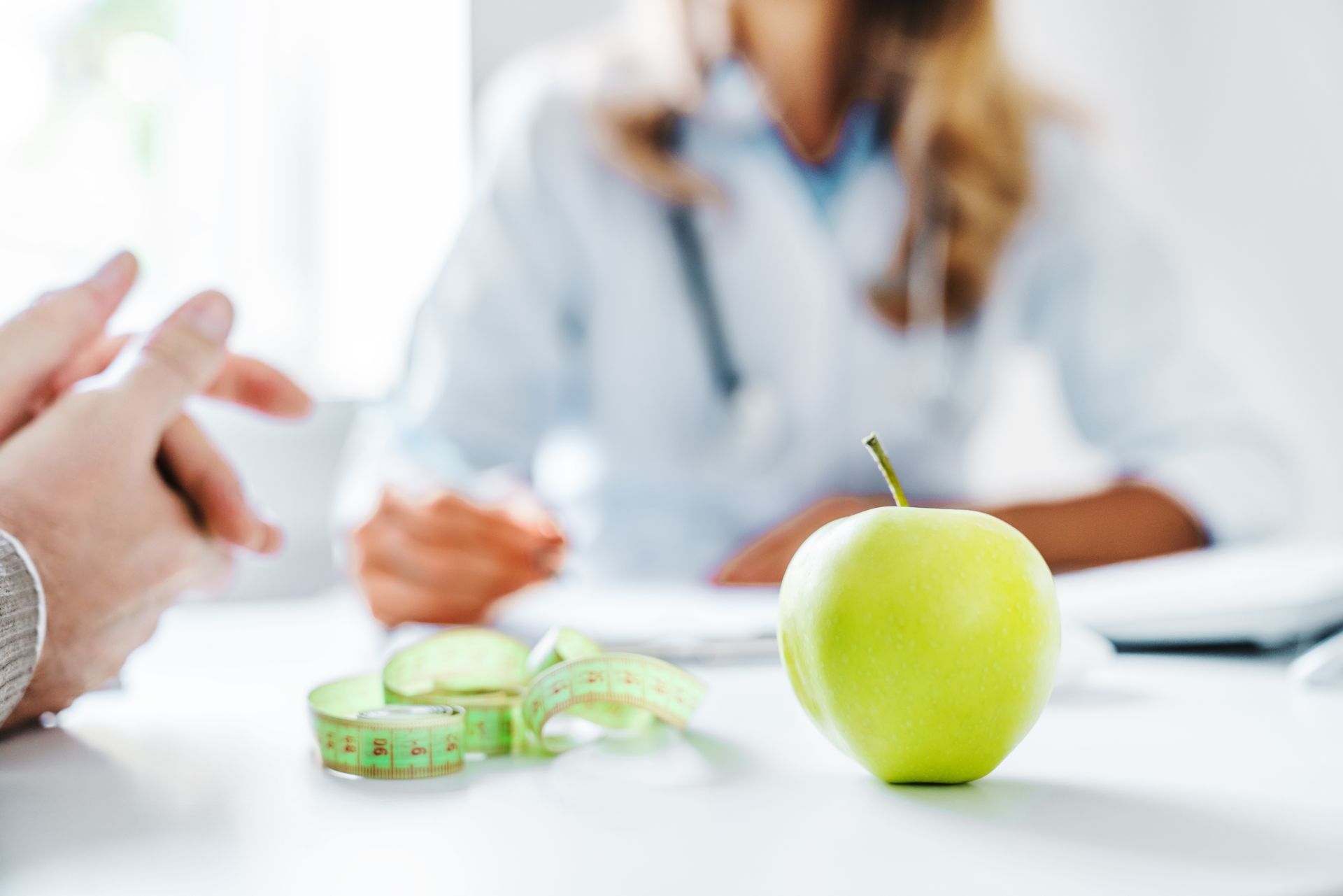 A blurred image of a female nutritionist sitting at a desk with a green apple