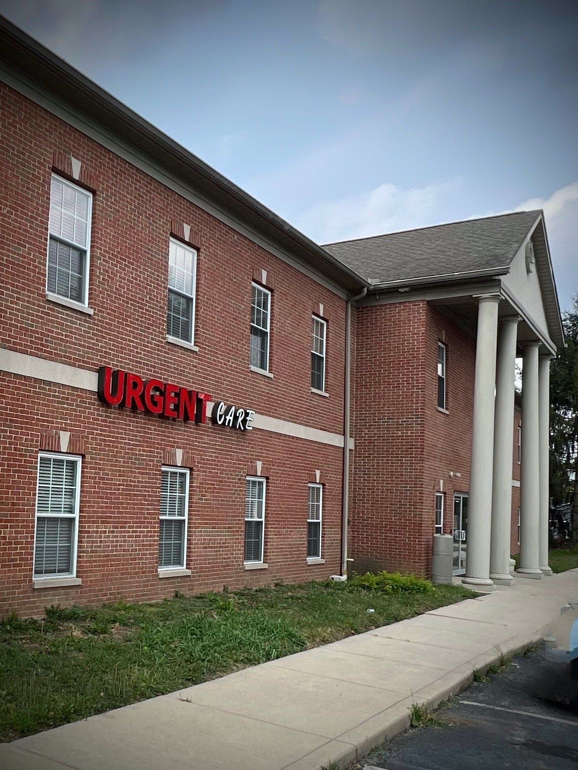 Exterior of an urgent care clinic with red and white lettering. Open 9-7. Building is brick with glass doors and windows.