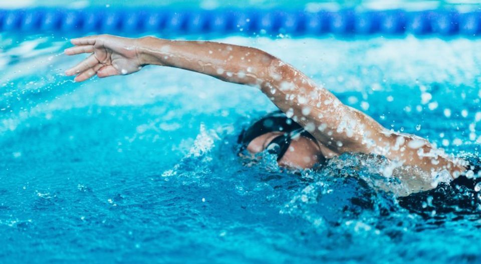 Swimmer in pool, performing the freestyle stroke, arm outstretched, splashing water.