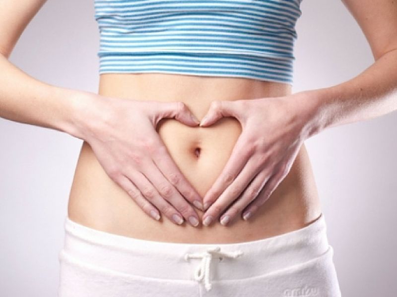 Woman in striped top and white pants making a heart shape over her abdomen.