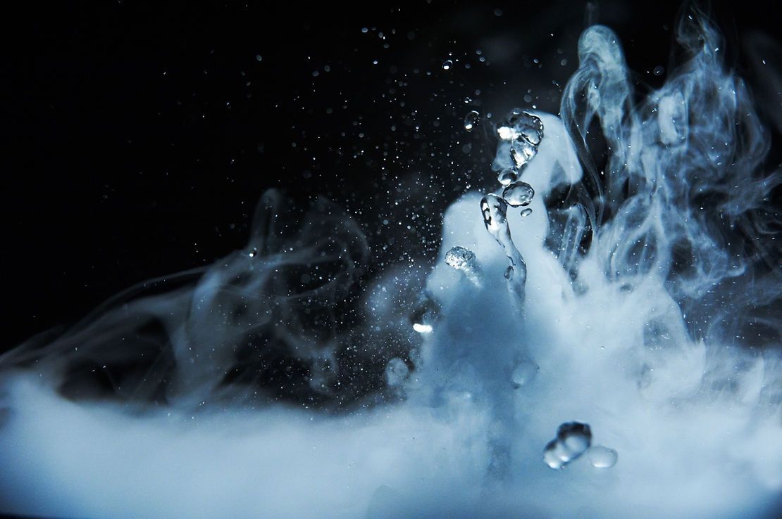Water droplets emerging from swirling white smoke against a black backdrop.