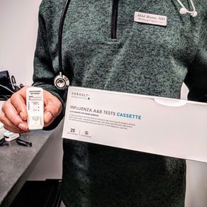 Doctor holding an influenza A&B test cassette and test kit; setting is a medical office.