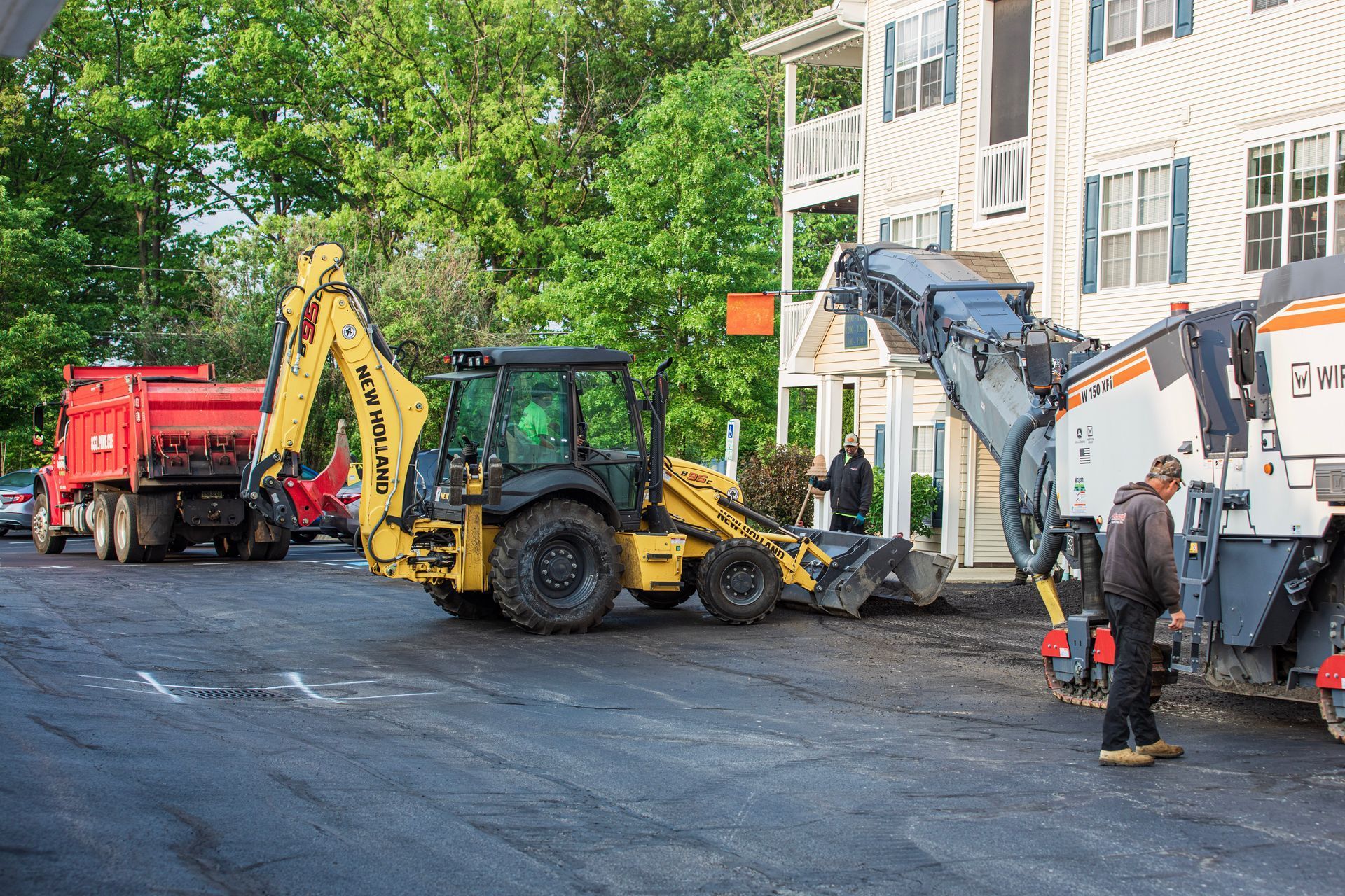 A group of construction vehicles are working on a parking lot in front of a building.