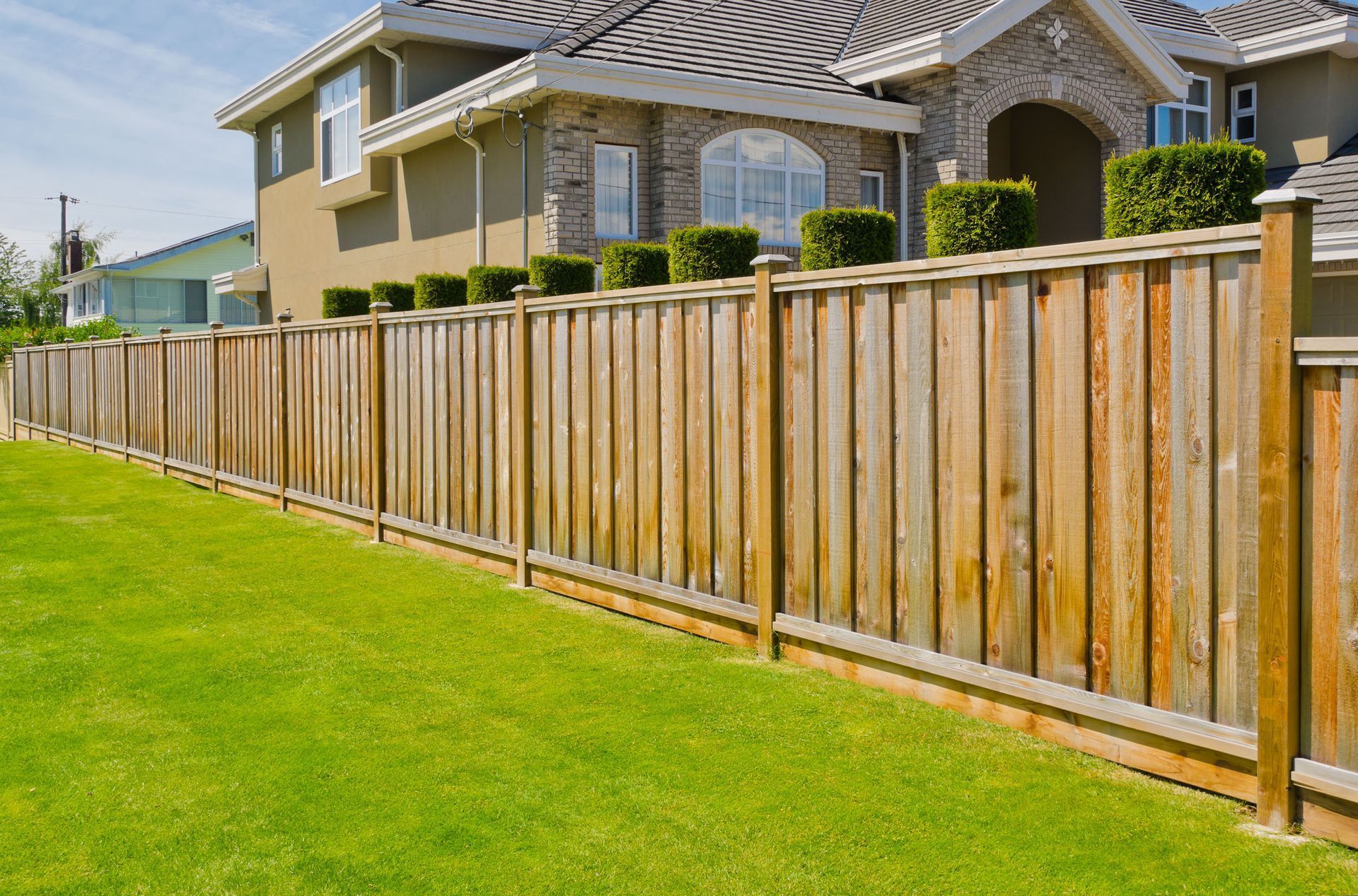 Wooden privacy fence beside a green lawn and suburban house under a clear sky