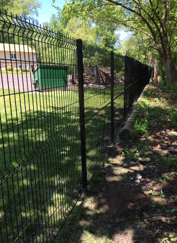 Black metal fence along a grassy path beside trees and a building on a sunny day