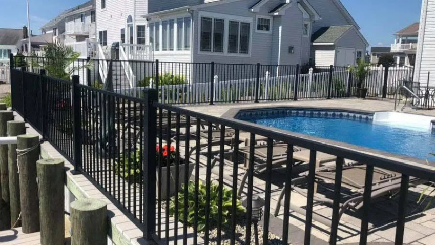 Apartment courtyard with black metal fence, patio tables, and a blue swimming pool under bright sunlight