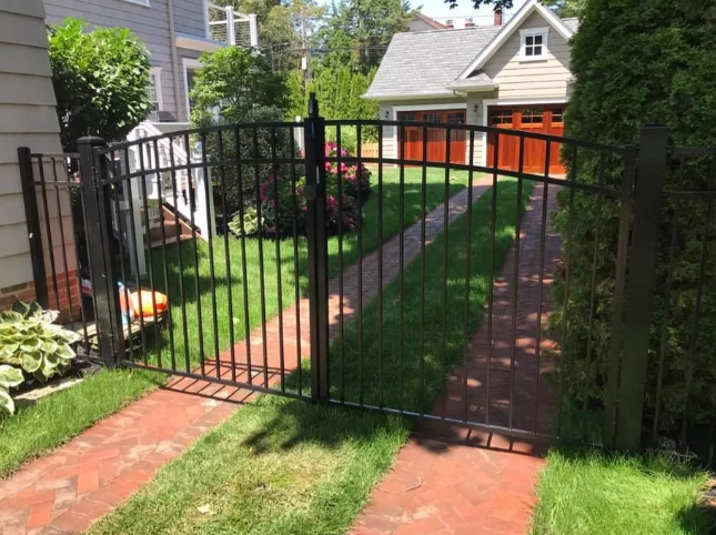 Black metal gate across a red-brick garden path with green lawn and house in the background