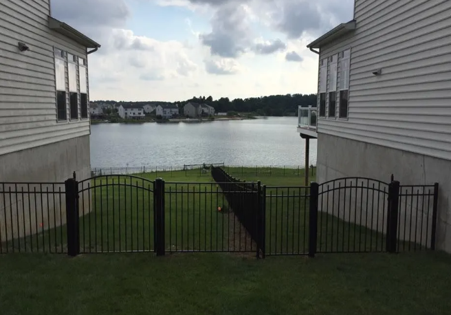 View between two gray houses of a lake, grassy yard, and black gate under cloudy sky