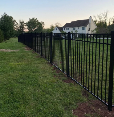 Black metal fence along a grassy yard with a white house in the background at dusk