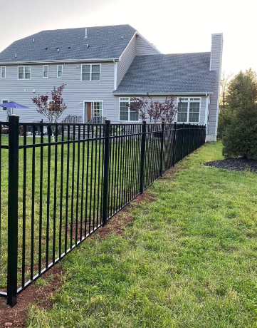 Black metal fence beside a green lawn in front of a gray house at dusk