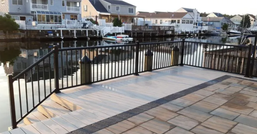 Harbor-side patio with black railings overlooking a canal and docked boats beside waterfront houses