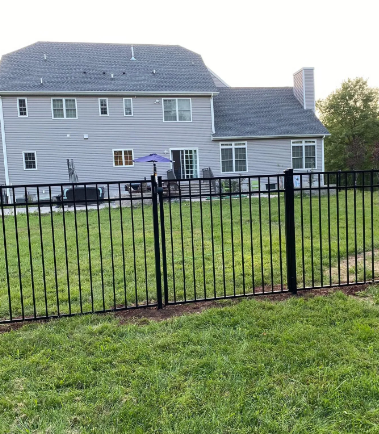 Black metal fence in front of a gray house with a backyard lawn and patio umbrella.
