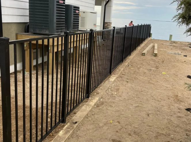 Black metal fence beside a white house along a sandy slope near the water