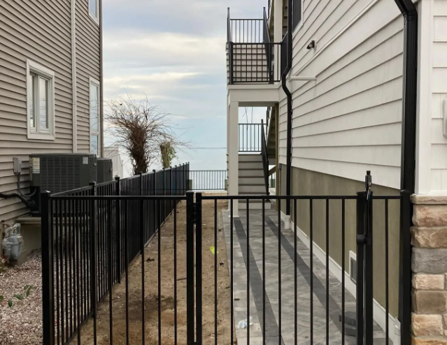 Black metal gate and narrow gravel walkway between two buildings beside a white-sided house.