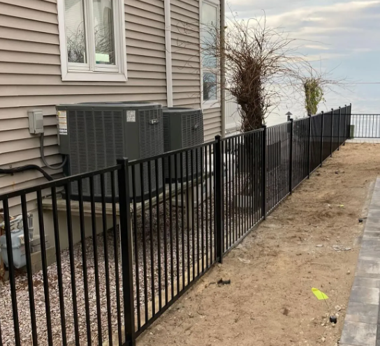 Black metal fence along a house exterior beside a sidewalk and dirt strip