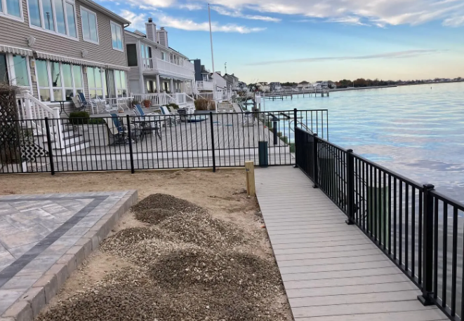 Waterfront townhouse patio with a black fence and narrow boardwalk beside calm water at sunset