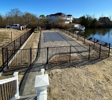 Fenced riverside patio with paved area and house in the background under clear skies