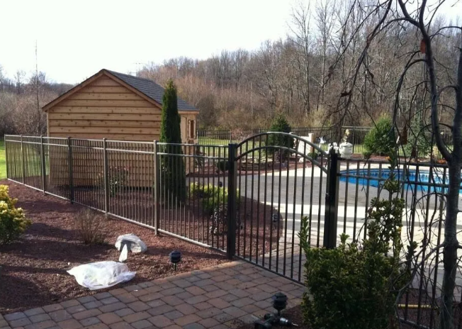 Backyard with metal fence, wooden shed, and above-ground pool beside a brick patio