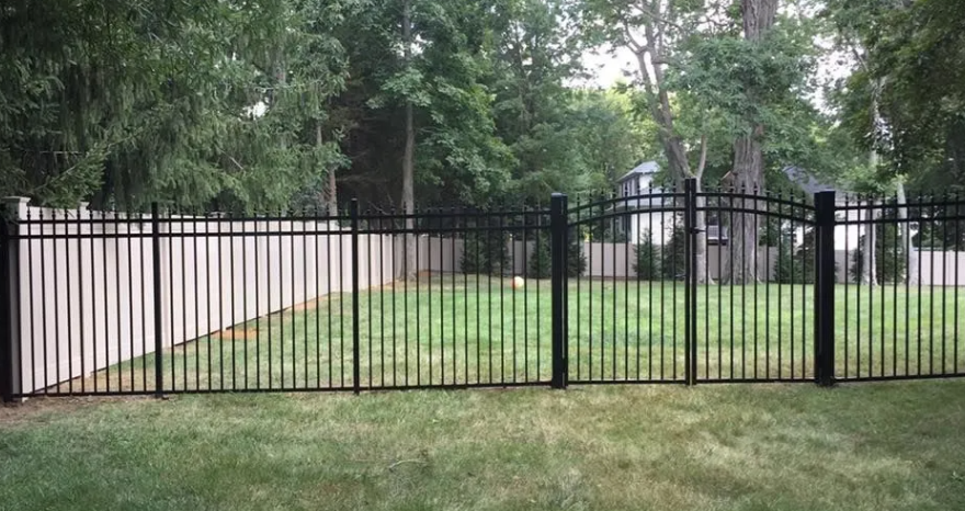 Black metal fence with gate in front of a grassy yard and trees