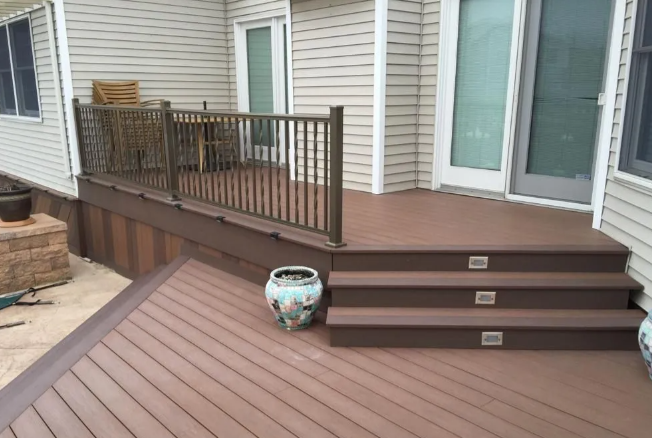Wooden deck with brown railings and steps beside a house, with a decorative planter on the lower deck