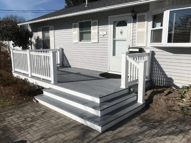 Front porch deck with white railings, gray steps, and a light-colored house exterior.