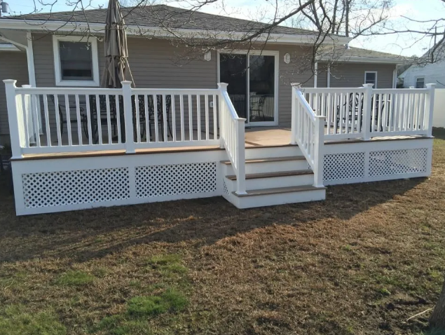 Front porch with white railings and steps on a beige house, set above a grassy yard.