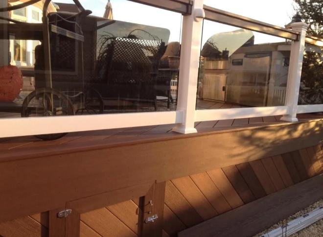 Wooden deck railing with wicker furniture visible through glass, lit by warm sunlight