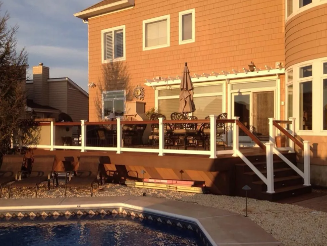 Backyard patio with deck, outdoor furniture, stairs, and pool beside a brick house