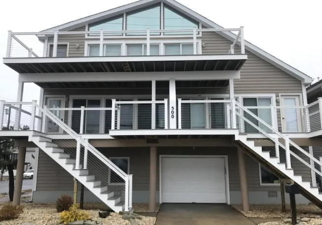 Gray beach house with wide front stairs, balconies, and a central garage below