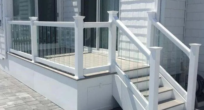 White porch ramp with glass railing and steps leading to a house entrance
