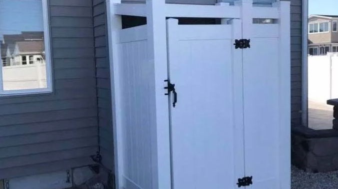 White outdoor storage shed beside a house, with black hinges and latch.