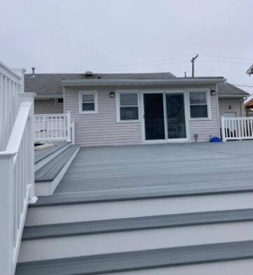 Backyard deck with gray boards and white railings facing a small gray house with sliding glass doors