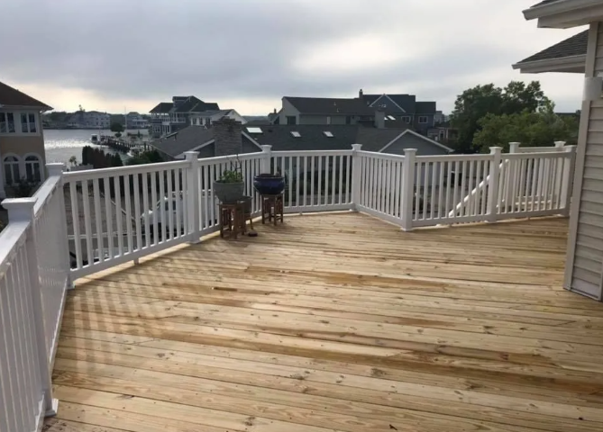 Wooden rooftop deck with white railings, two stools, and neighboring houses in view
