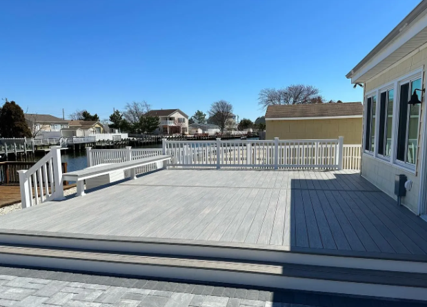 Wide white deck with railings outside a house, overlooking a waterfront neighborhood under a clear sky
