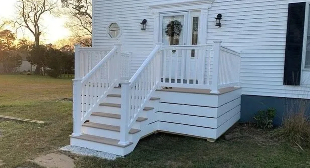 White house entrance with small porch steps, railing, and deck; lawn and sunset in background