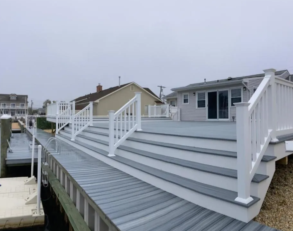 White outdoor stairs and deck on a waterfront house with gray siding and neighboring homes nearby