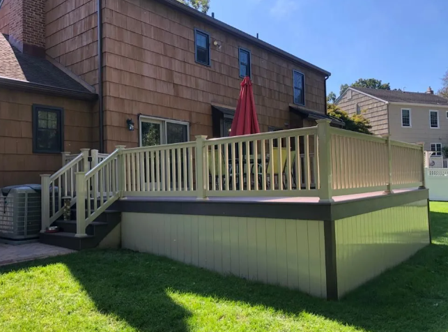 Back deck with cream railing, red umbrella, and stairs beside a brick house