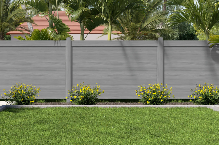 Gray fence with tropical plants, small yellow flowers, and green lawn in front