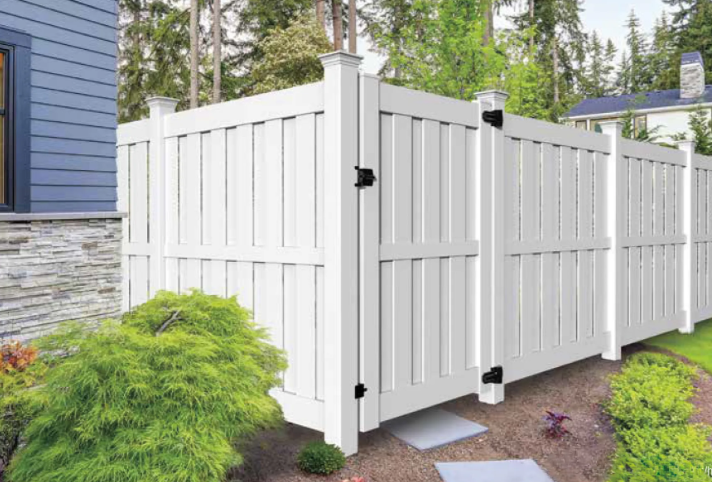 White vinyl privacy fence and gate beside a blue house and landscaped yard