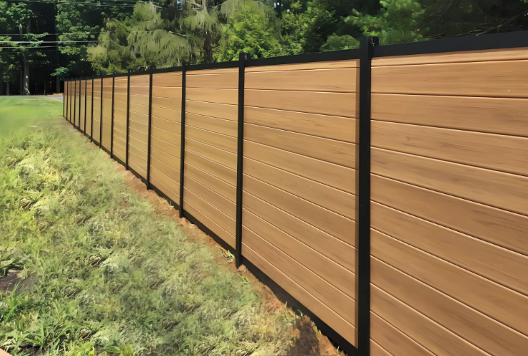 Long brown wooden privacy fence along a grassy yard beside trees