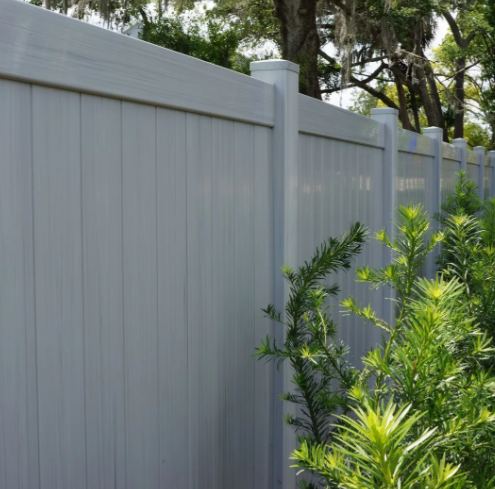Light gray vinyl privacy fence with green shrubs in front and trees behind