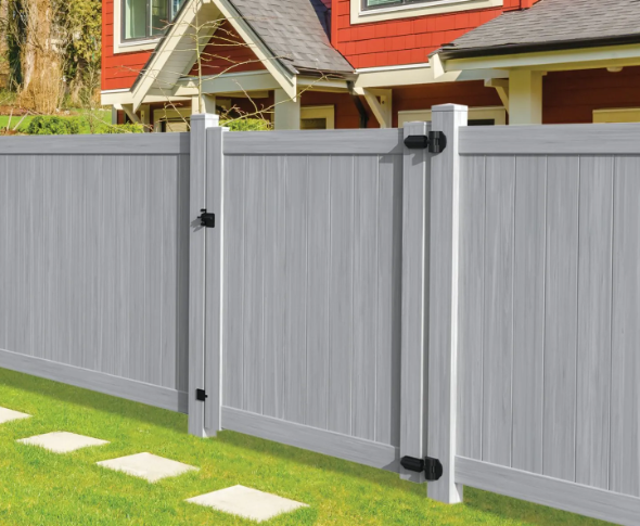 Gray vinyl privacy fence with two gates in a backyard beside a red house and lawn stepping stones